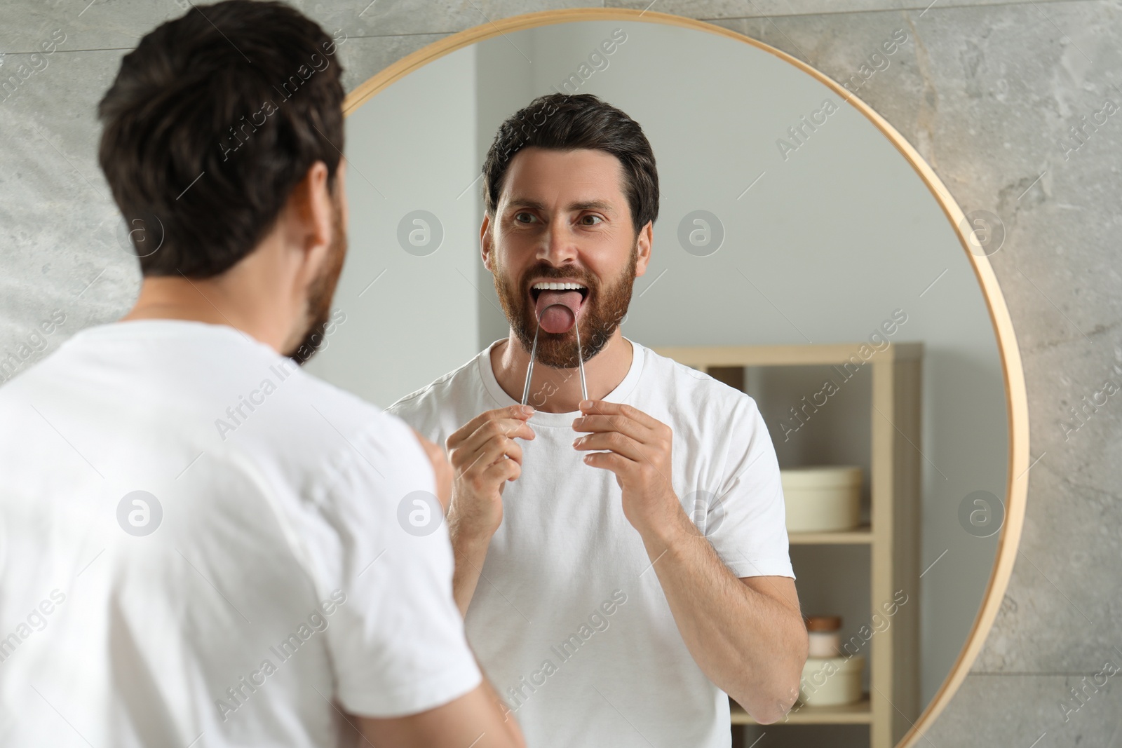 Photo of Handsome man brushing his tongue with cleaner near mirror in bathroom