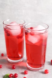 Tasty cranberry juice with ice cubes in glasses and fresh berries on light grey table, closeup