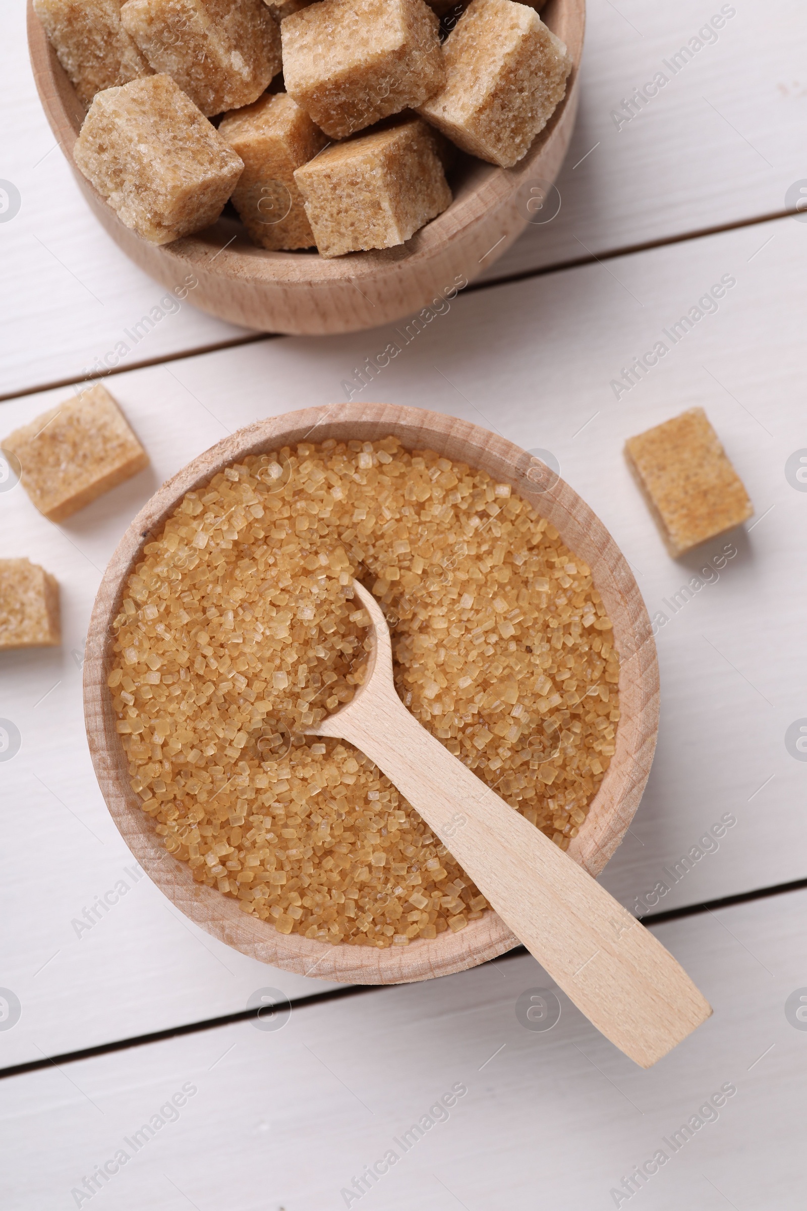 Photo of Bowls and spoon with different types of brown sugar on white wooden table, flat lay