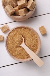 Photo of Bowls and spoon with different types of brown sugar on white wooden table, flat lay