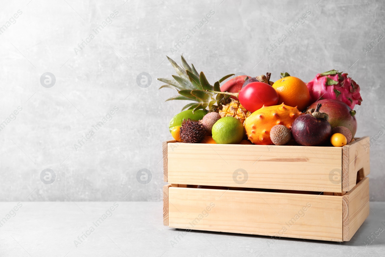 Photo of Crate with different exotic fruits on light grey table. Space for text