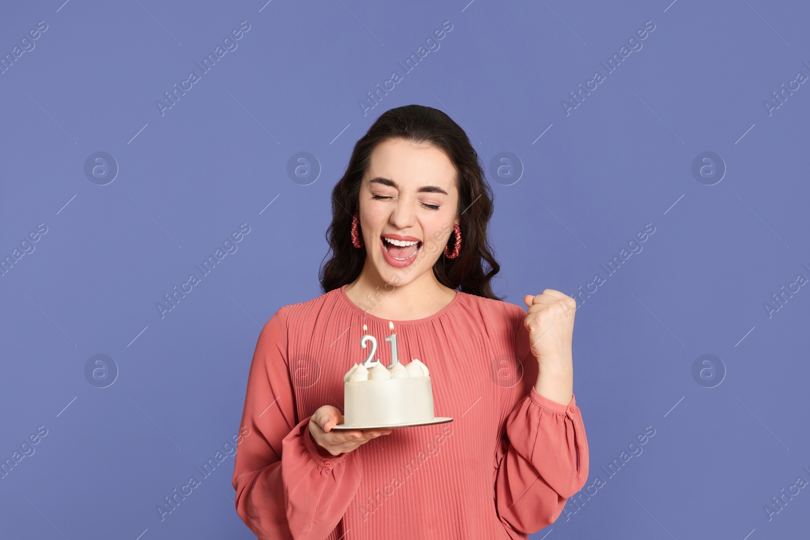 Photo of Coming of age party - 21st birthday. Excited woman holding delicious cake with number shaped candles on violet background