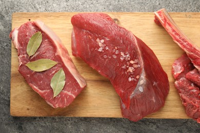 Photo of Pieces of raw beef meat and spices on grey textured table, top view