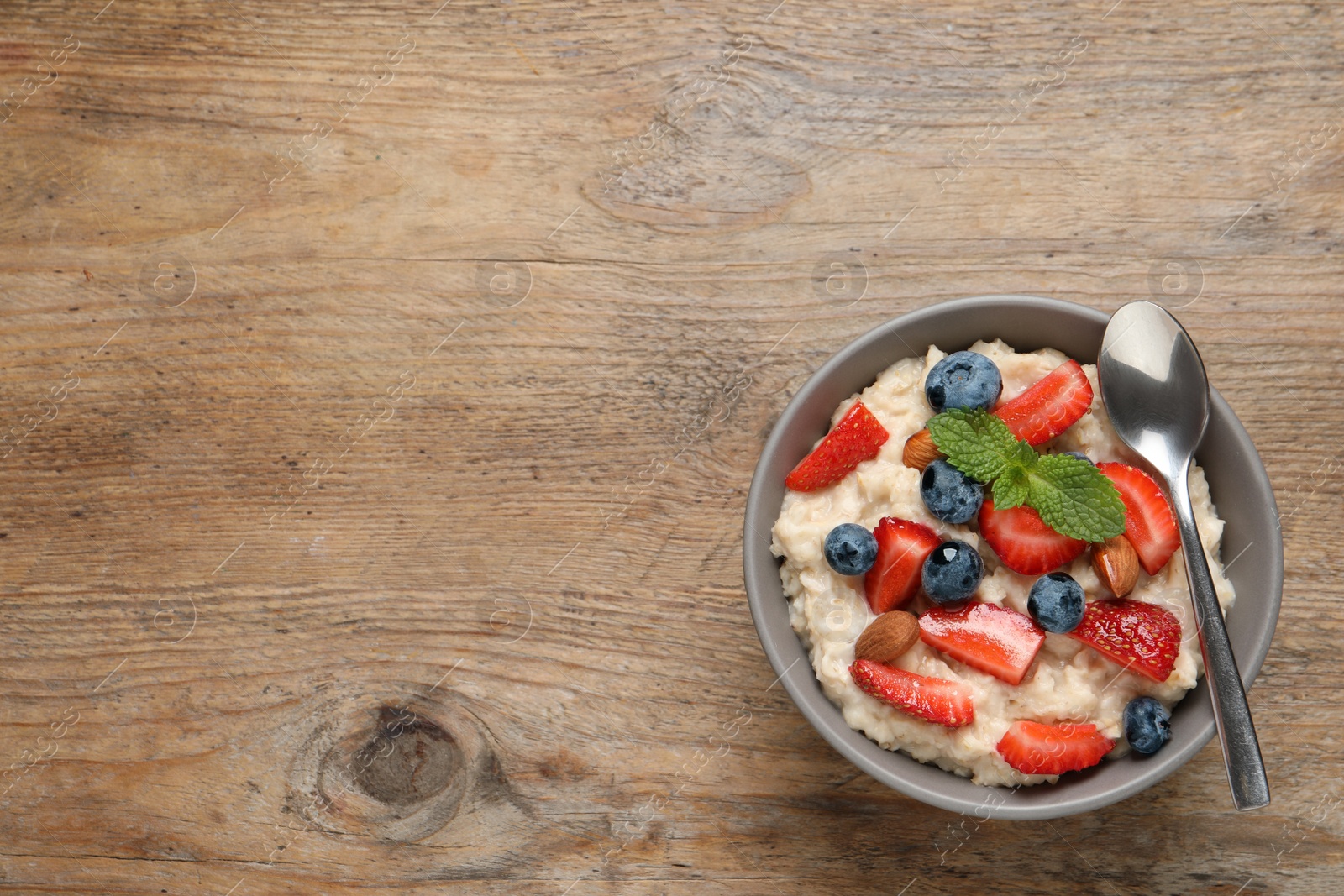 Photo of Tasty oatmeal porridge with berries and almond nuts in bowl on wooden table, top view. Space for text