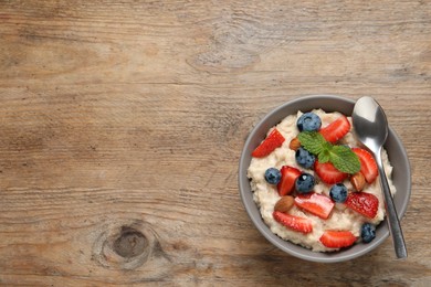 Tasty oatmeal porridge with berries and almond nuts in bowl on wooden table, top view. Space for text