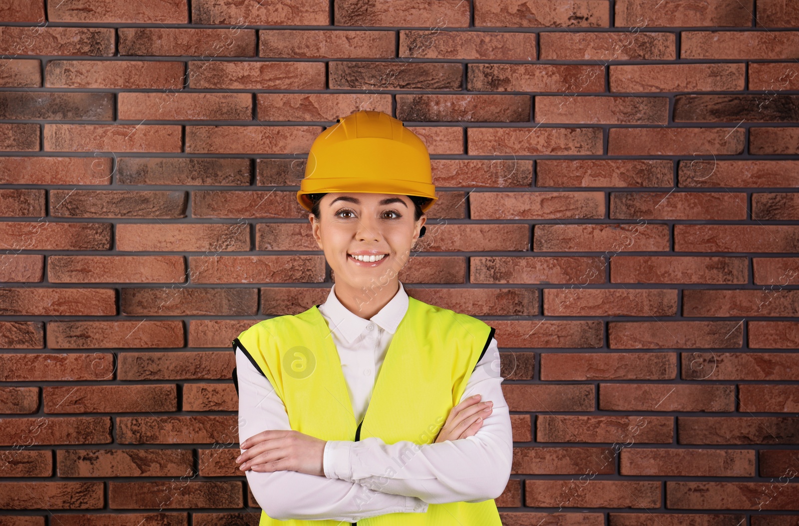 Photo of Female industrial engineer in uniform on brick wall background. Safety equipment