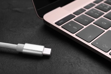 Photo of USB cable with type C connector and laptop on black slate table, closeup