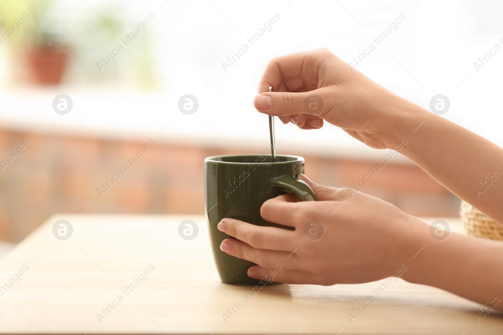 Photo of Woman stirring tea with spoon at table indoors, closeup. Space for text