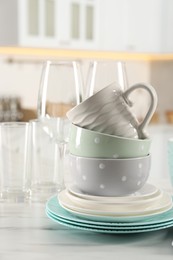 Photo of Many different clean dishware, cups and glasses on white marble table in kitchen, closeup