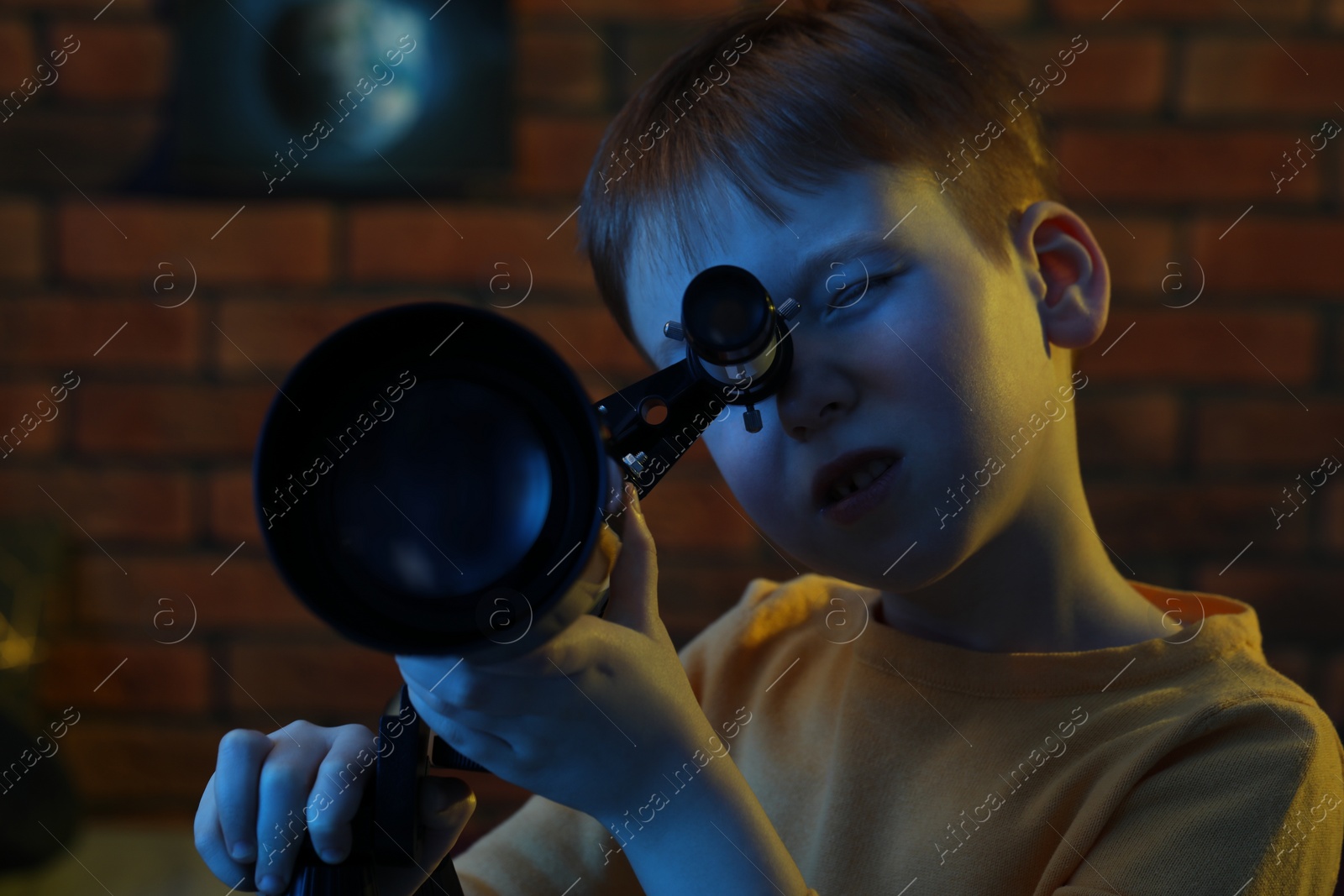 Photo of Little boy looking at stars through telescope in room