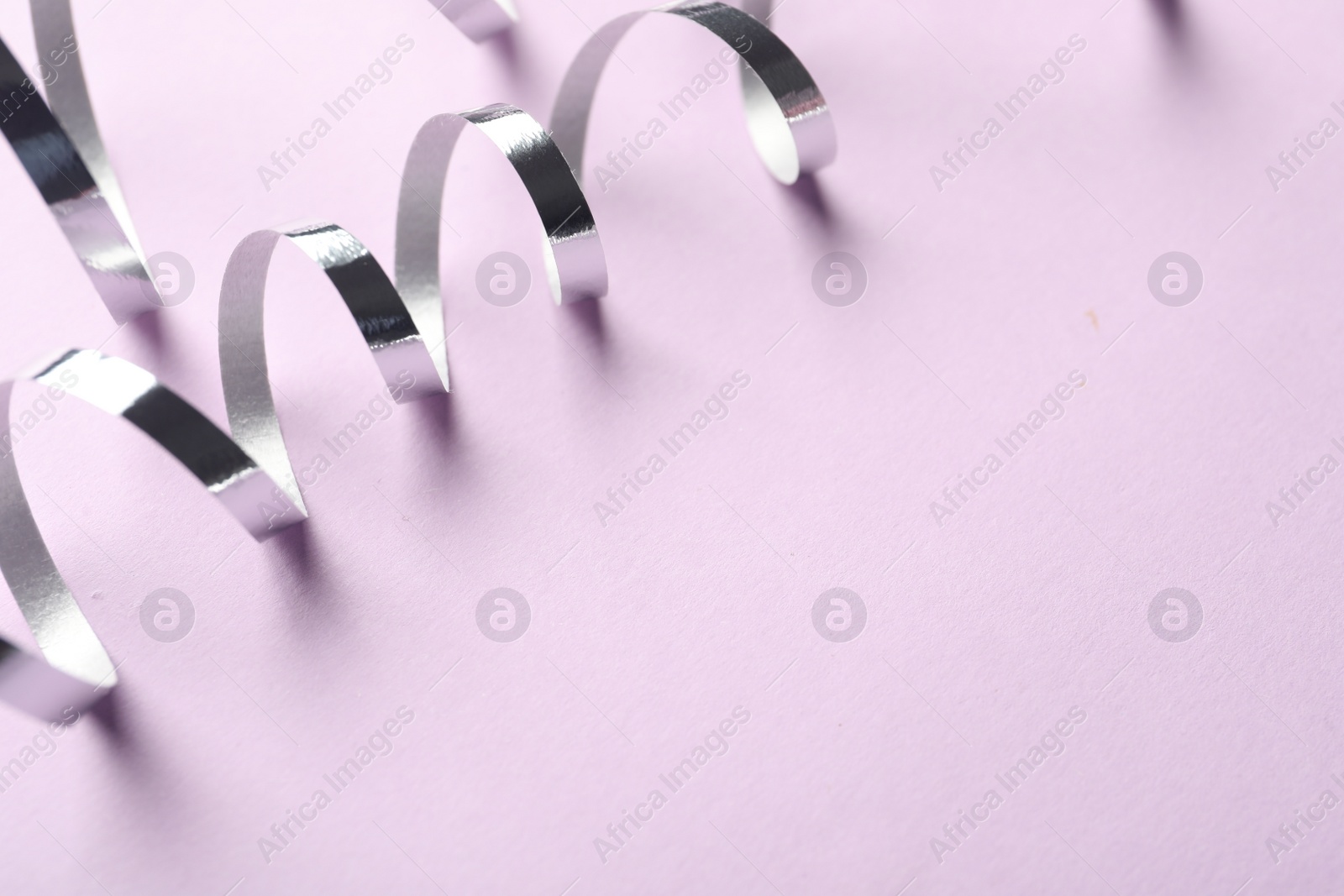 Photo of Shiny serpentine streamers on lilac background, closeup. Space for text