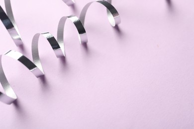 Photo of Shiny serpentine streamers on lilac background, closeup. Space for text