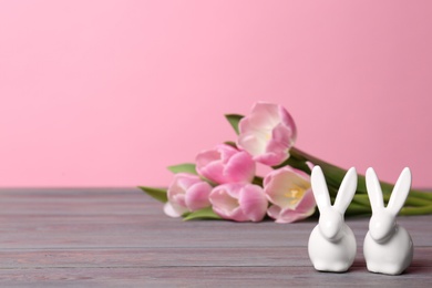 Cute ceramic Easter bunnies and spring tulips on wooden table against color background, space for text