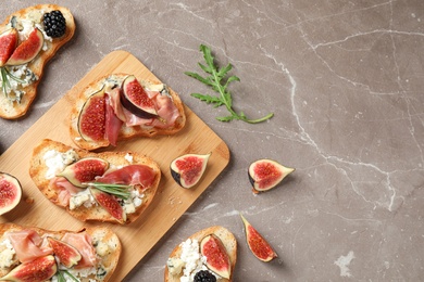 Photo of Bruschettas with cheese, prosciutto and figs on marble table, top view. Space for text