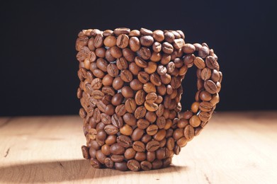 Photo of Cup made of coffee beans on wooden table against black background