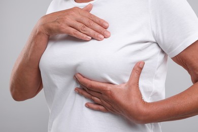 Photo of Woman doing breast self-examination on light grey background, closeup