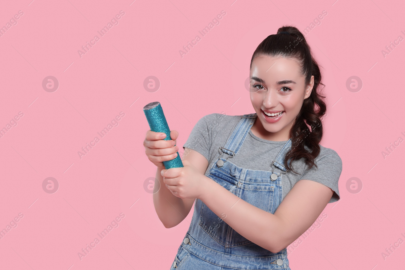 Photo of Young woman blowing up party popper on pink background, space for text