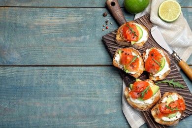 Photo of Delicious sandwiches with cream cheese, salmon, avocado and arugula served on light blue wooden table, flat lay. Space for text