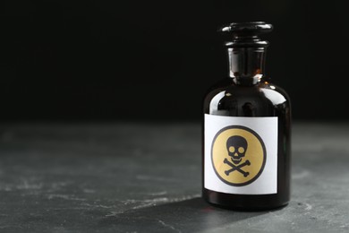 Photo of Glass bottle of poison with warning sign on black table. Space for text
