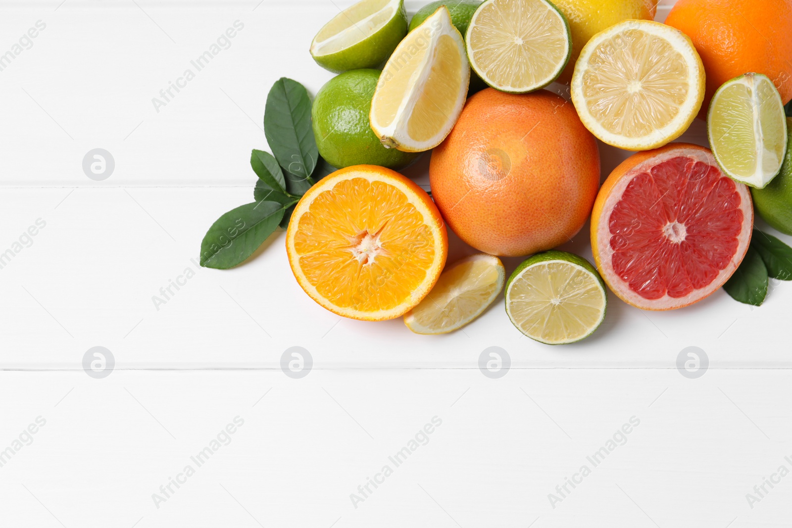 Photo of Different fresh citrus fruits and leaves on white wooden table, flat lay. Space for text