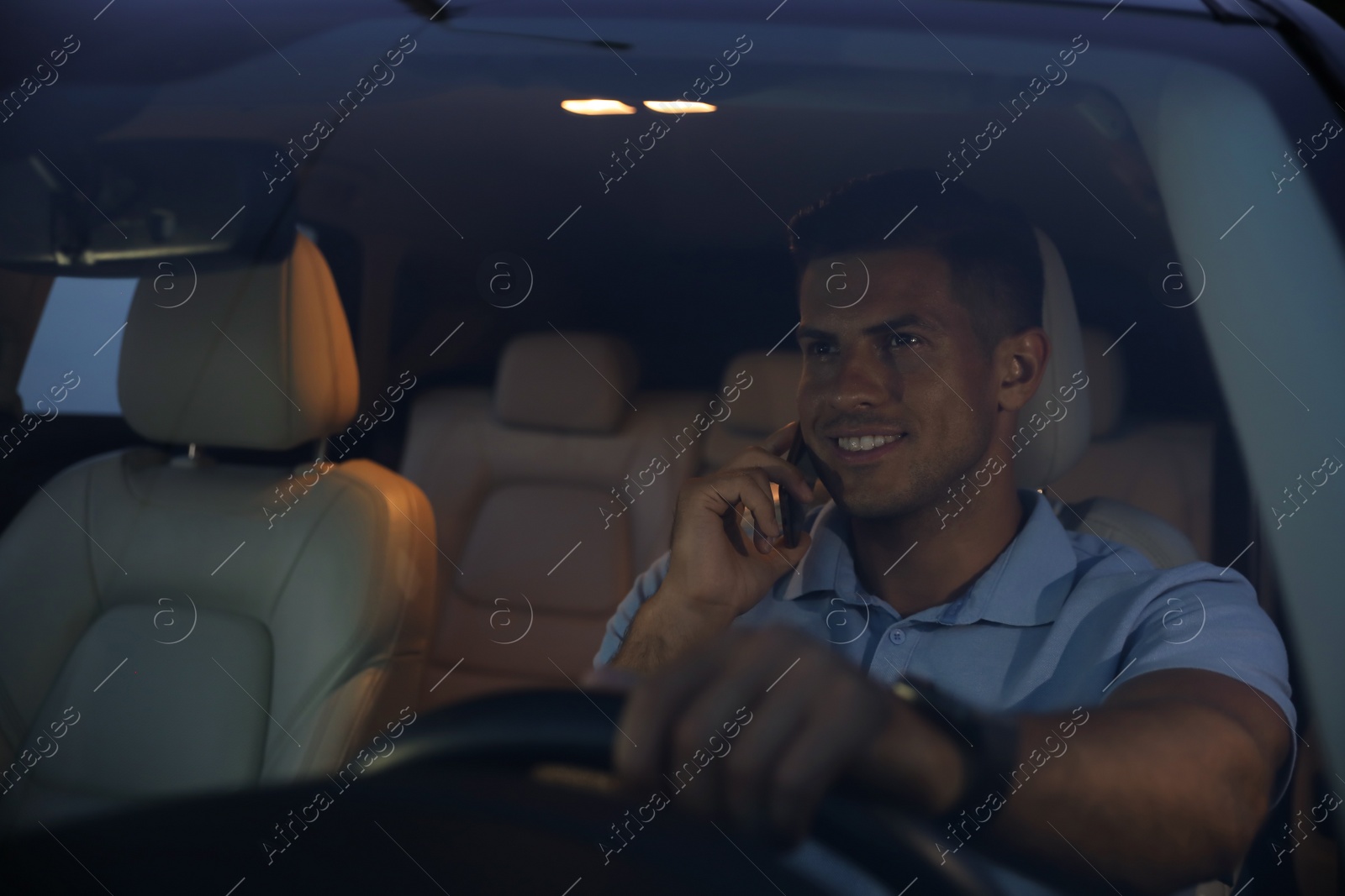 Photo of Handsome man talking on phone while driving his modern car