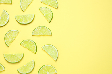 Photo of Juicy fresh lime slices on yellow background, flat lay. Space for text