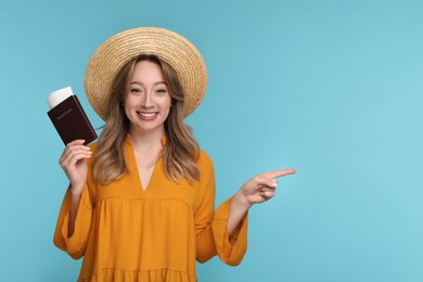 Photo of Happy young woman with passport, ticket and hat pointing at something on light blue background, space for text