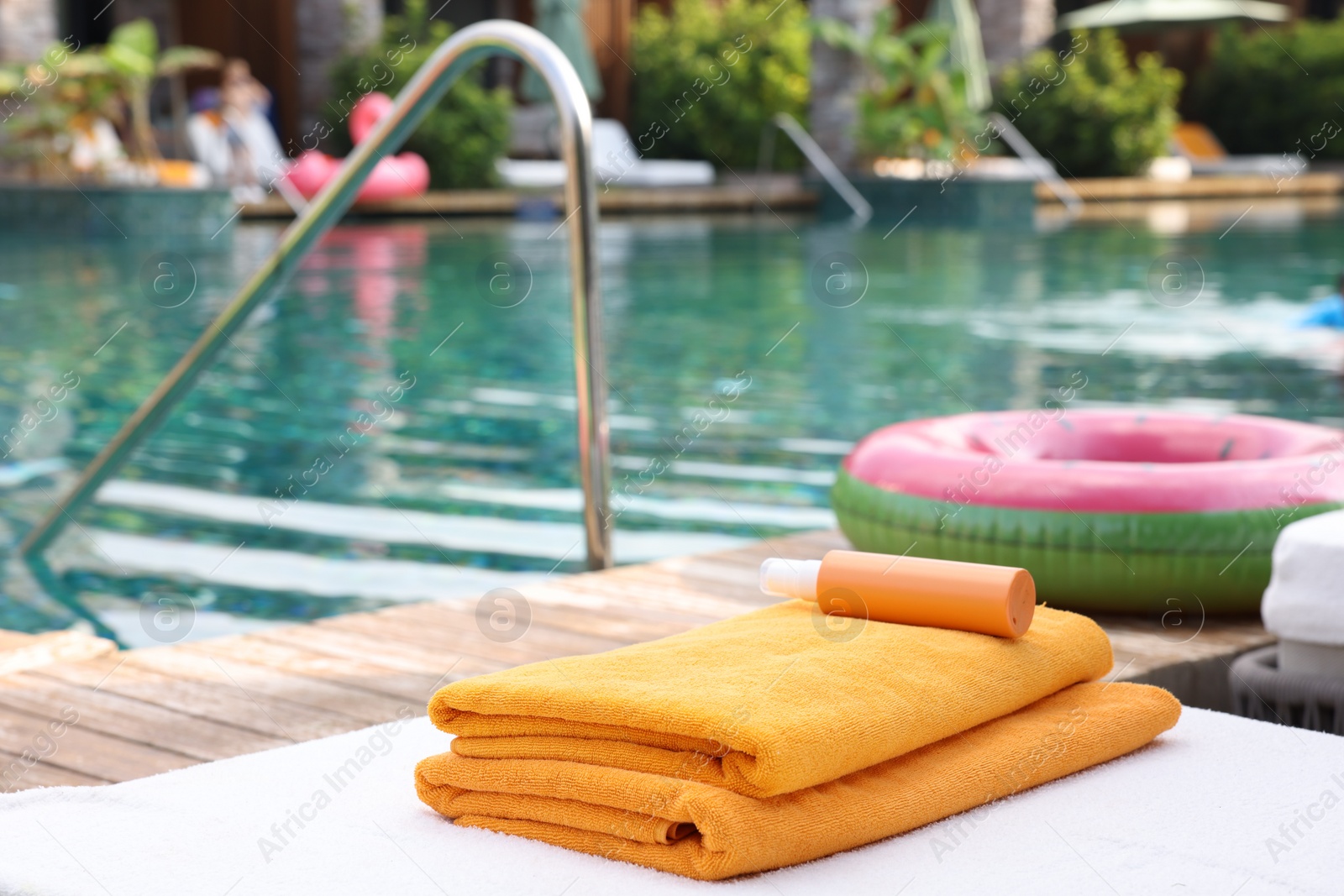 Photo of Beach towels and sunscreen on sun lounger near outdoor swimming pool at luxury resort, selective focus. Space for text