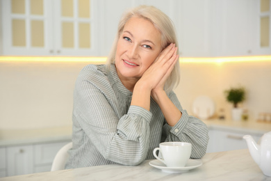 Photo of Beautiful mature woman with cup of coffee in kitchen