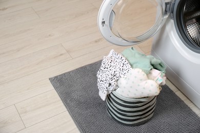 Laundry basket with baby clothes and bedding near washing machine in bathroom. Space for text