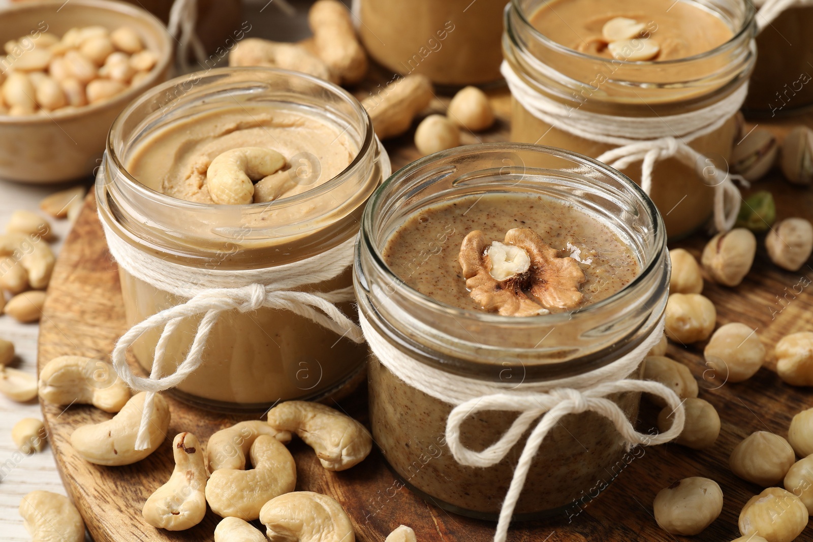 Photo of Tasty nut butters in jars and raw nuts on table, closeup