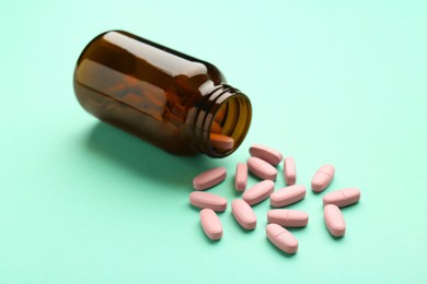 Photo of Vitamin pills and bottle on mint color background, closeup