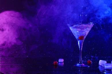 Martini splashing out of glass near ice and cherries in neon lights, space for text