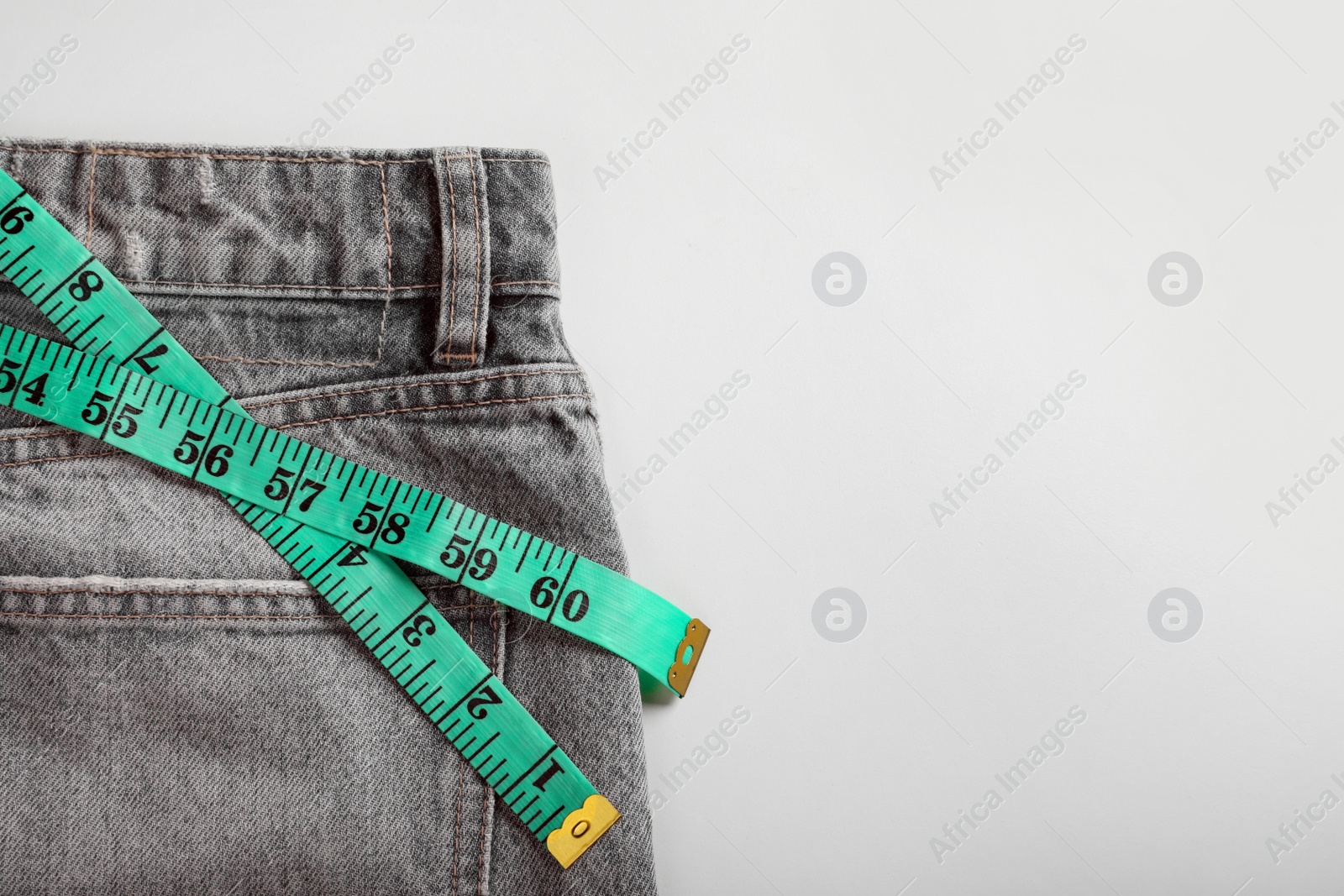 Photo of Jeans with measuring tape on light grey background, top view and space for text. Weight loss concept