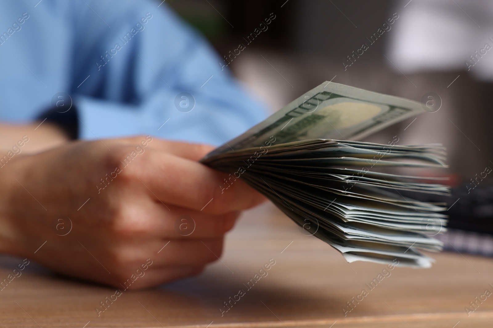 Photo of Money exchange. Woman holding dollar banknotes at wooden table, closeup