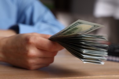 Money exchange. Woman holding dollar banknotes at wooden table, closeup