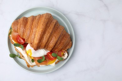 Tasty croissant with fried egg, tomato and microgreens on white table, top view. Space for text