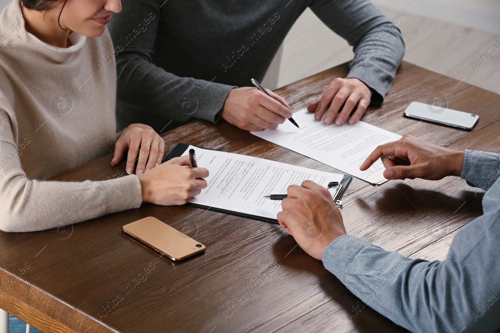 Photo of Notary helping couple with paperwork at wooden table, closeup