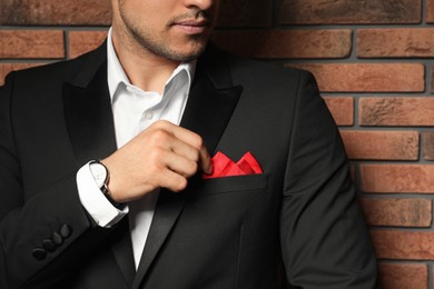 Photo of Man fixing handkerchief in breast pocket of his suit near brick wall, closeup