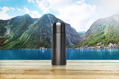 Wooden desk with thermos and mountain landscape on background