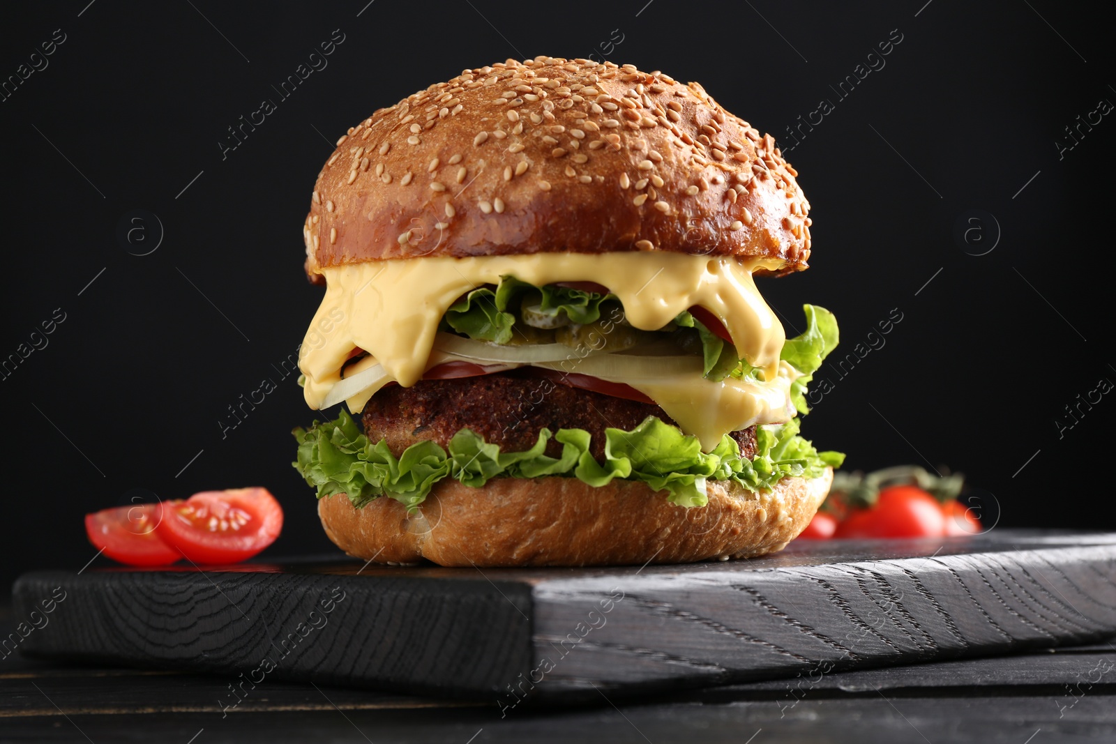 Photo of Vegetarian burger with delicious patty on black wooden table, closeup