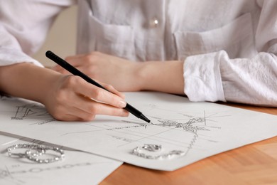 Photo of Jeweler drawing sketch of elegant necklace on paper at wooden table, closeup