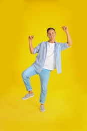 Happy attractive man dancing on yellow background