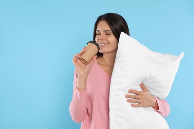 Happy young woman with soft pillow drinking coffee on light blue background