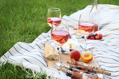 Photo of Glasses of delicious rose wine and food on picnic blanket outdoors