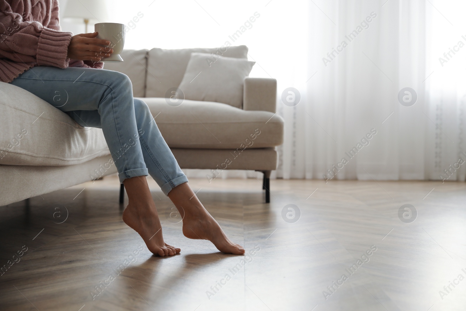 Photo of Barefoot woman sitting on sofa in living room, closeup. Floor heating system