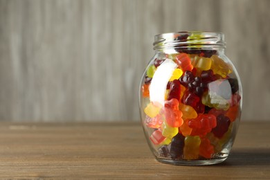 Photo of Delicious gummy bear candies in jar on wooden table. Space for text