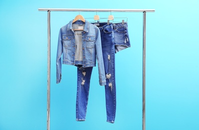 Photo of Rack with stylish jeans and denim clothes on color background