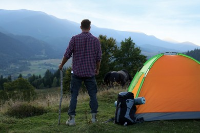 Photo of Tourist with backpack and sleeping pad near camping tent in mountains