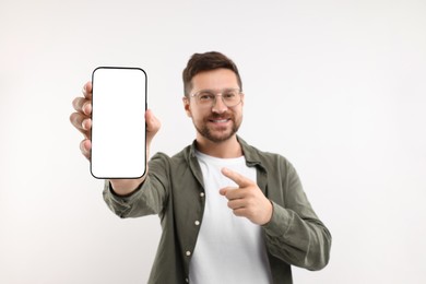 Handsome man showing smartphone in hand and pointing at it on white background, selective focus. Mockup for design